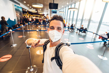 Man wearing protective face mask taking selfie portrait at terminal airport - Happy tourist waiting...