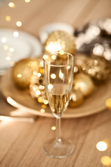 Christmas table setting with holiday decorations in a gold color. New Year celebration. Glass of champagne.