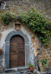 Fototapeta na wymiar Tuscany, Italy, May 2018, an ancient door in a stone wall entwined with ivy in the medieval city of Civita
