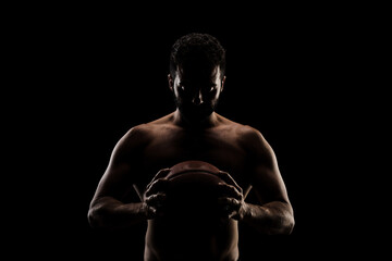 Fototapeta na wymiar Basketball player holding a ball against black background. Side lit muscular Caucasian man silhouette