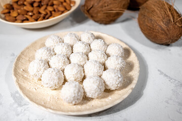 White sweet coconut candies in plate, coconuts and almond nuts, ingredients on background, close up with selective focus