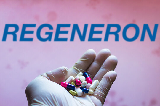 November 27, 2021, Brazil. In this photo illustration a Regeneron Pharmaceuticals logo is seen on a screen and a hand holding pills.