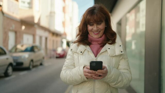Middle age redhead woman smiling confident using smartphone at street