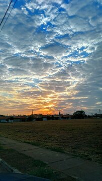 Blue sky with colorful clouds. Rising sun. Park with green grass and houses in the background. C&eacute;u azul com nuvens colorida. Sol nascente. Parque com grama verde e casas ao fundo.