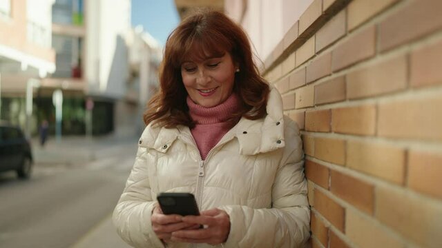 Middle age redhead woman smiling confident using smartphone at street