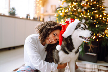 Happy woman celebrating winter holidays with a dog Husky on the background of the Christmas tree. New year. Christmas surprise.