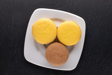 Three sweet macaroons on a white saucer on a slate stone, close-up, top view.