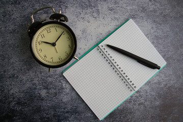 Open notepad with a pen and alarm clock on the gray background