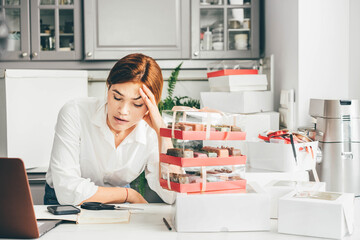 Process of packing cookies into a cardboard kraft box. Woman feeling bored, frustrated and sleepy after work. Small business owner.