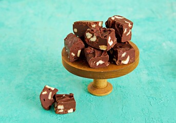 Sliced homemade fudge chocolates made from dark chocolate, condensed milk and hazelnuts on a wooden stand on a turquoise concrete background. Candy recipes. American cuisine.