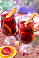 two glasses of mulled wine, a garland in the background. Grog with cinnamon, orange and berries. Winter New Year's drink