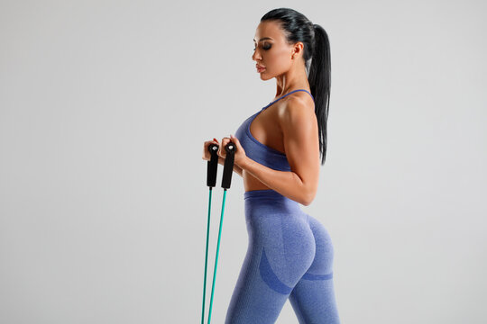 Fitness woman working out with resistance band on gray background. Athletic girl exercises with expander