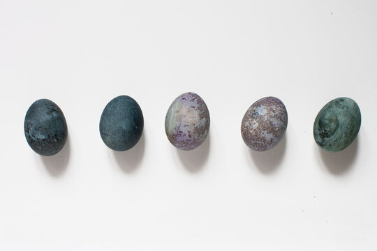 isolated idea shot on white background of a row of five Easter eggs painted with natural paint looking like cosmic planets and galaxies in space