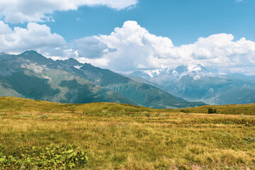 Fototapeta premium Summer mountain landscape in Svaneti region, Georgia, Asia. Snowcapped mountains in the background. Blue sky with clouds above. Georgian travel destination