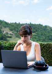 Young woman teleworking with a worried face, using her laptop in a rural area.
