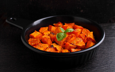 Pumpkin cut into pieces baked in a black round frying pan with a handle on a black background.