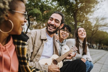 Group of best friends hanging out on city downtown - Happy guys and girls having fun together playing guitar outside - Happy lifestyle and friendship concept - obrazy, fototapety, plakaty