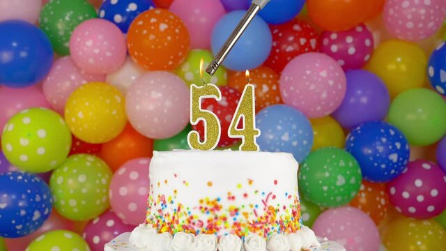 Candles on the celebration cake. Candles in the form of number 54. Birthday cake and colorful balloons in the background.