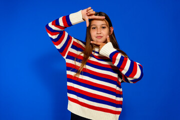 Adolescent girl in a striped sweater making the gesture of being framed by a camera. She practices...