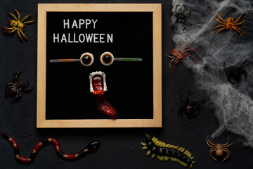 spider web, snakes, insects made of candy and marmalade on a black background, Halloween, top view. happy halloween text