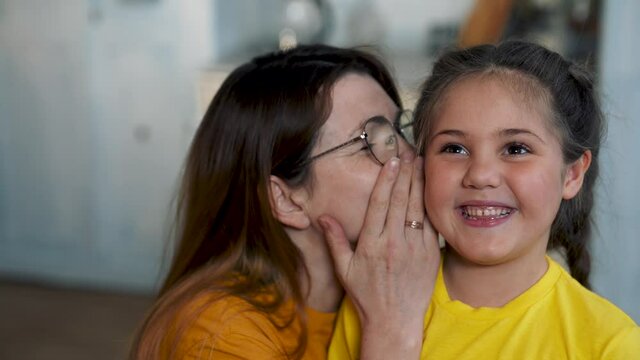 Mom and daughter are happy family. Girl whispers secret to her mother in her ear. Mom communicates with her daughter. Happy family concept. Mom whispers a secret in girl ear. Family games and fun.
