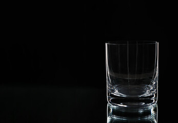 Glass tumbler empty on a black background. New empty whiskey glass on black background.