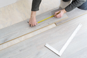 DIY, repair, building and home concept - close up of male hands lying parquet floor board/laminate flooring