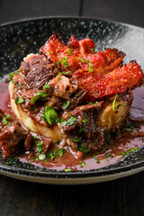 Closeup view of beef goulash with bacon chips, mashed potato and black currant sauce