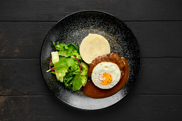 Overhead view of beef cutlet with fried egg, mashed potato and fresh salad