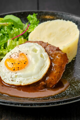 Closeup view of beef cutlet with fried egg, mashed potato and fresh salad