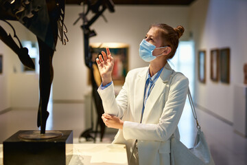 Woman visitor wearing an antivirus mask in the historical museum looking at pictures.