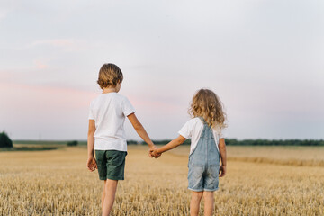 brother and sister in a mowed field of wheat holding hands, the concept of the relationship of children in the family