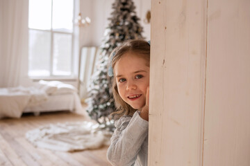 a little girl in a blue lace dress is playing hide and seek behind a white door in a room