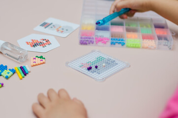Children's educational game aqua mosaic, a small child inserts multicolored beads into the pattern...