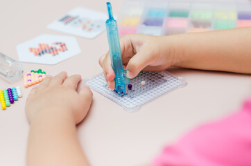 Children's educational game aqua mosaic, a small child inserts multicolored beads into the pattern with a special pen.