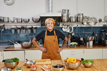 Portrait of smiling female cook looking at camera while posing in industrial kitchen interior, copy space