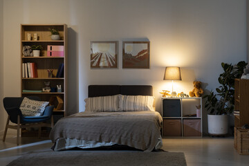 Cozy bedroom interior at night: stripped bed linen, nature pictures on wall, wooden shelves and...