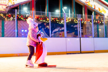 A little girl is skating on an ice rink, holding on to a support, a child is learning to skate,...