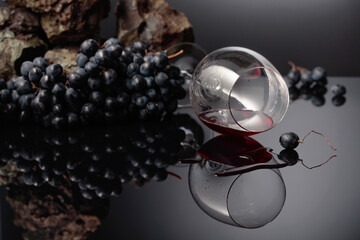 Blue grapes and wine glass with red wine on a black reflective background.