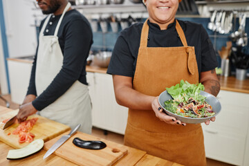 Cropped shot of female cook holding bowl with vegetable salad while working in professional kitchen, copy space