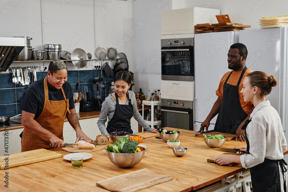 Wall mural diverse group of people laughing while cutting vegetables together in cooking class, copy space