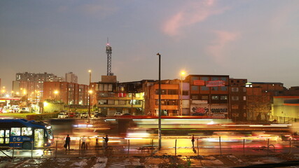 Avenida en Bogotá y viviendas al atardecer, llega el autobus.