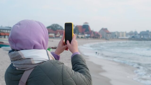 Woman blogger in warm clothes does selphie on the winter beach. Traveller at the cold sea in the off-season, 4k 60p