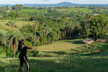 Mulher passeando pelo campo em meio a muitas árvores frutíferas e uma linda paissagem em volta 