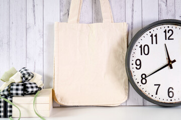 Tote bag product mockup. New Year's Eve farmhouse theme SVG craft product mockup styled with large rustic clock, stack of books and buffalo plaid ribbon agasint a white wood background.