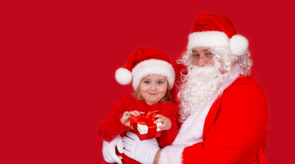 Smiling little girl in a hat with Santa Claus and gifts, isolate on a red background. Holidays, childhood and the concept of people