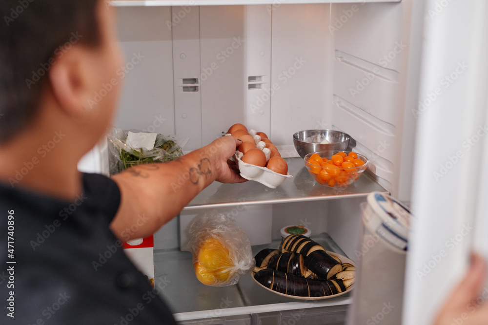 Wall mural back view portrait of unrecognizable woman taking fresh eggs out of refrigerator in kitchen, copy sp