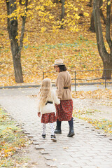 Mom and daughter are walking in beautiful colored dresses family look in an autumn park with leaves