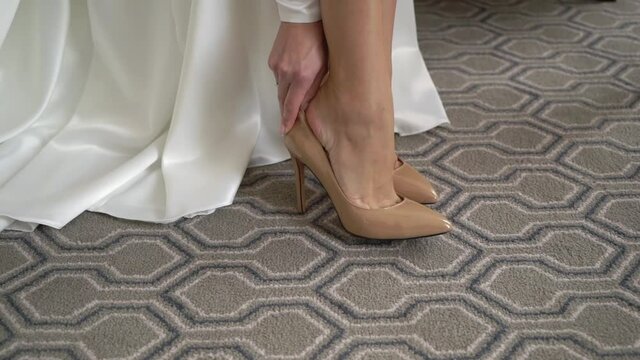 Young woman bride wears beige wedding shoes with heels. A girl in a wedding dress gets dressed in the morning before the ceremony.