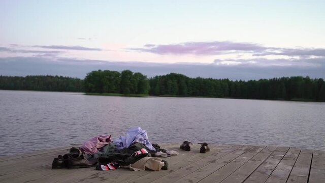 Clothes and shoes are on the pier. People undressed and swim naked in the lake in the evening at sunset or at night, skinny dipping. There are no people, only a shirt and pants. Naturist bathing.
